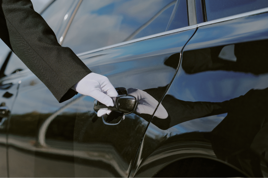 戴白色手套、穿西裝的專業包車司機準備幫客戶拉開後座車門